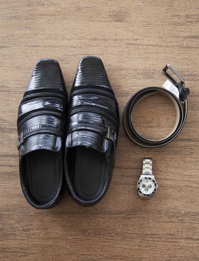 An overhead shot of male black shoes with a belt and a watch on a brown surface