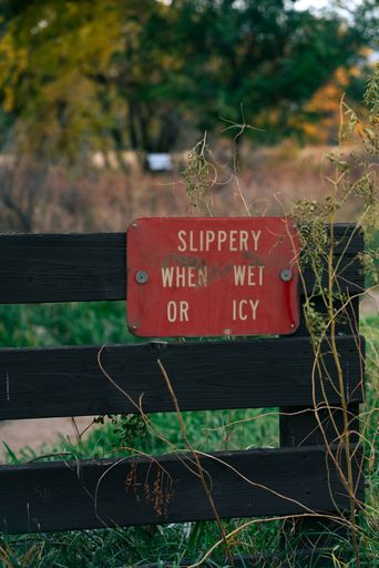 The vertical view of a slippery floor warning sign on a wooden fence in the greenery