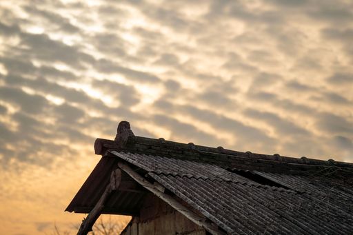 A low angle shot of a rural wooden house rooftop against a cloudy sky at sunset