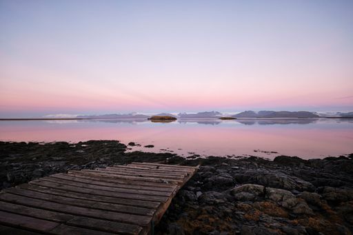 A beautiful pink sunset reflecting on the surface of a lake with wooden stairs on the shore, Hofn, Iceland