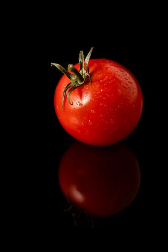 A vertical closeup of a fresh ripe tomato isolated on the black background.
