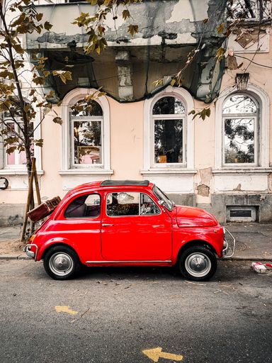 A vertical shot of an old red Fiat 500 parked on the street