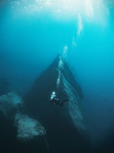 A vertical shot of a scuba diver exploring Gozo reefs swimming near the giant rocks