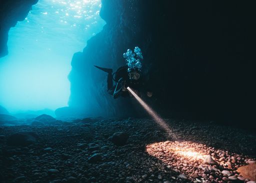 A scuba diver exploring the underwater reefs by illuminating the stones with the help of a flashlight