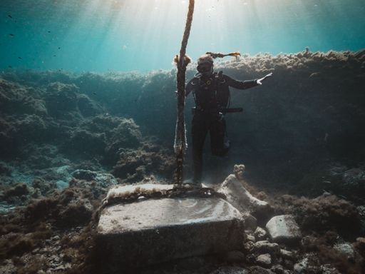 A closeup shot of a scuba diver swimming near an ancient find surrounded by algae