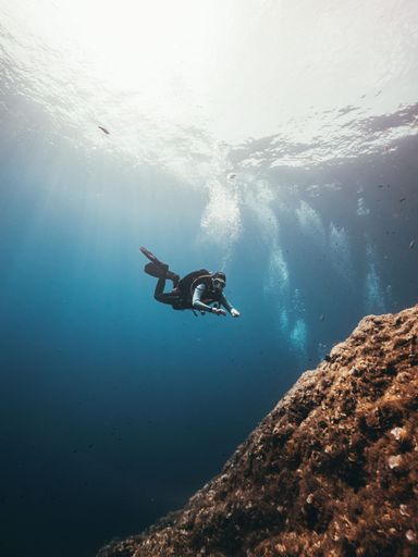 A vertical shot of a scuba diver exploring reefs, swimming near the giant rocks
