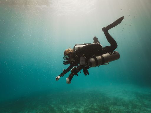 A rebreather technical diver on the sunlit ocean diving deeper, corals blurred background