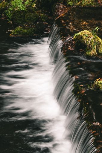 A long exposure shot of the cascade waterfall surrounded by the mossy rocks in the forest