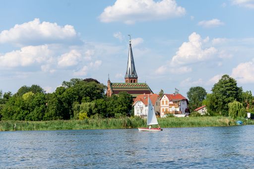 he village church of Geltow with its colourful roof, photographed from the water. In the foreground you can see a sailboat.