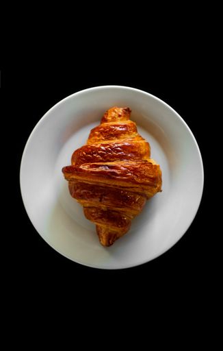 A vertical shot of a croissant on a plate on a black background