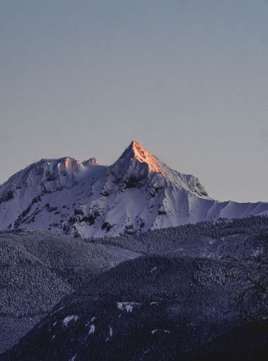 A vertical shot of a snow-covered mountain peak during sunrise