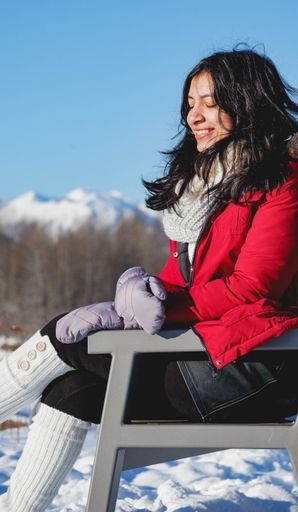 A beautiful vertical portrait of a female wearing a winter warm outfit sitting on a bench