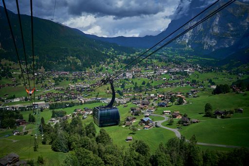 A gondola riding above the green field, buildings and mountains of Switzerland