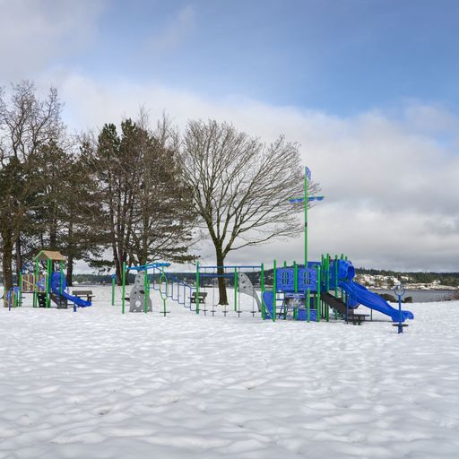 An empty children's playground beside the ocean in a snow covered park on a bright winter day.