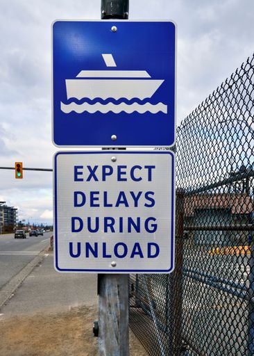 A blue and white sign stating 'expect delays during unload'