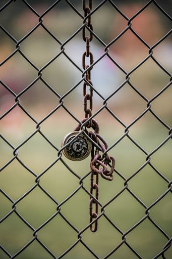A vertical closeup of a lock hanging on a chain-link fence against a blurred background
