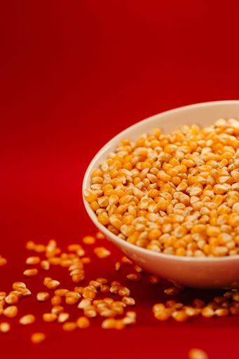A vertical closeup of a popcorn bowl with some corns spilled around it isolated on a red background