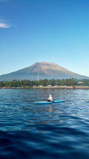 An aerial view of a person in a kayak floating on the water near the volcano in Bali, Indonesia