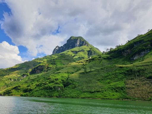 A scenic shot of a mountain covered in green grass under a cloudy blue sky