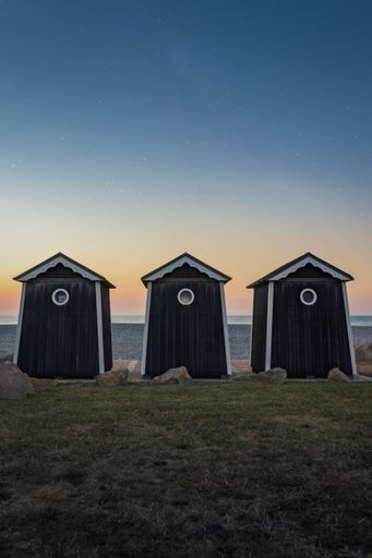 Vertical shot of wooden beach houses in Normandy region in northern France. Green meadow under night sky with stars. Blue hour