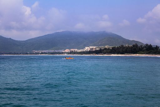 Blue calm seascape with a small banana boat and the beach under the cloudy blue sky