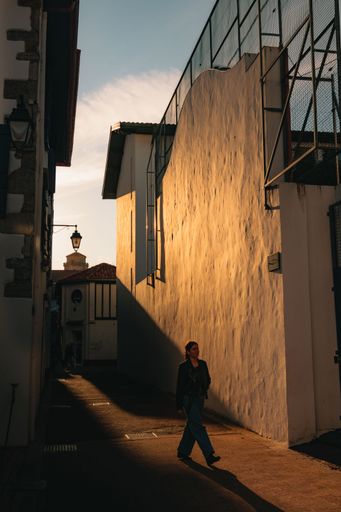 A vertical shot of the Caucasian stylish girl walking on the street between the buildings at sunset