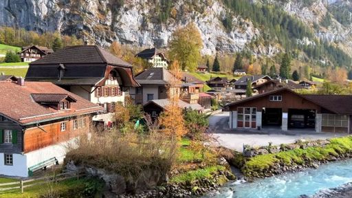 A scenic view of traditional cozy houses near a river surrounded by mountains in Lauterbrunnen village