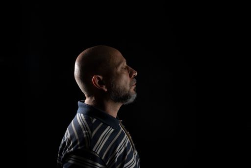 A bald man with beard wearing a casual shirt over black background, full of Thoughts
