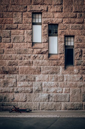 A vertical shot of scooter on the side of a street with brick walled background