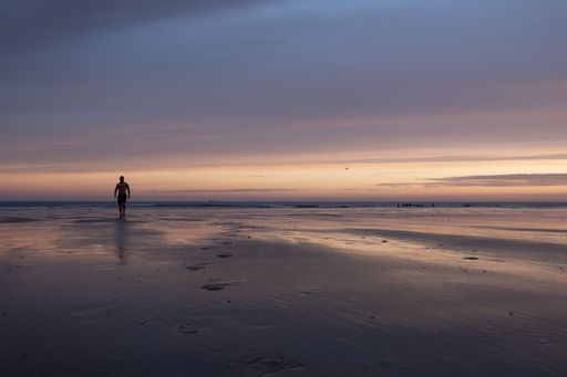 A silhouette of a man walking on the sandy beach with the sea and the sunset in the background