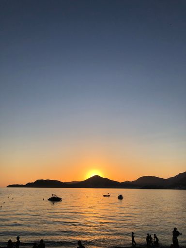 A vertical shot of the golden sunset shining behind the mountains over the calm waters of the sea