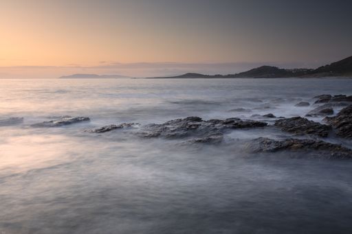 A mesmerizing shot of ocean waves crashing on the rocks with mountains in the background