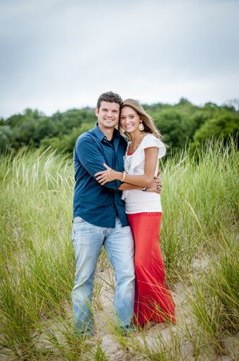 A vertical shot of a couple standing in a grassy field while hugging and smiling at the camera