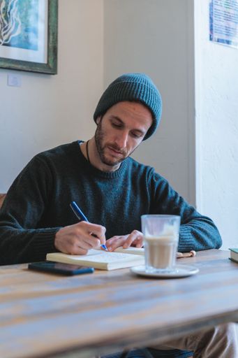 A young man writing in the notebook with the coffee on wooden table