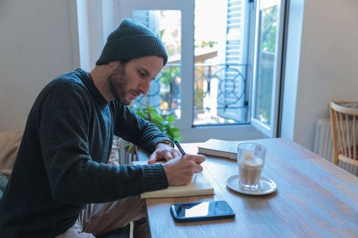 A young man writing in the notebook with the coffee on wooden table