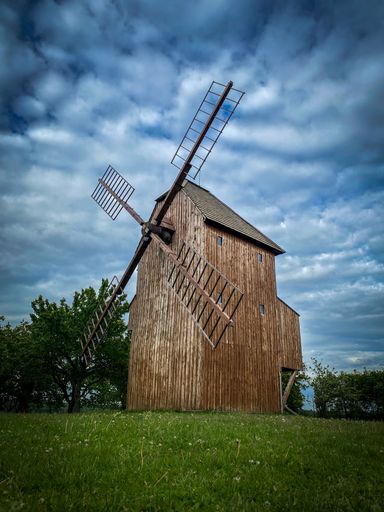 A vertical shot of a wooden windmill on a cloudy day in a rural area