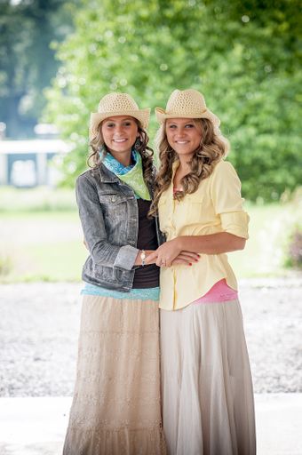 Two smiling women in hats and colorful dresses in a park under sunlight with a blurry background