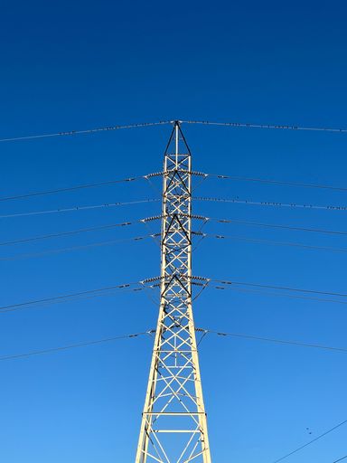 A vertical shot of an electric tower with a blue sky in the background