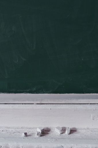 A vertical shot of a dirty blank blackboard with white pieces of chalk on the stand
