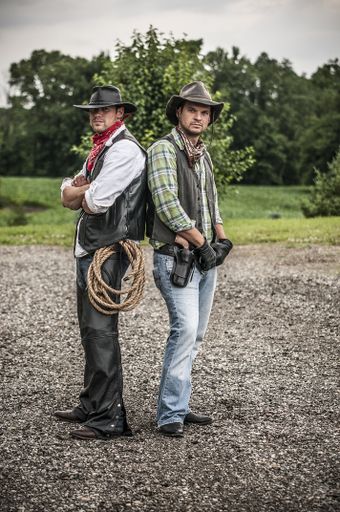 A vertical shot of two males wearing a cowboy outfit while standing back to back