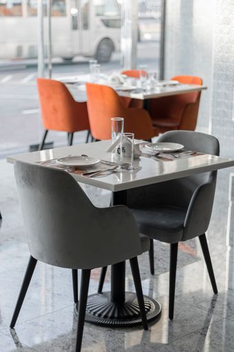 A vertical shot of grey and orange chairs and cutlery on the table in the restaurant.