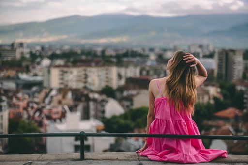 A woman in a pink dress sitting and looking at the city.