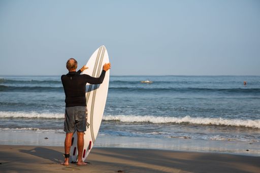 The man with a surfboard standing on the beach and looking at the sea.