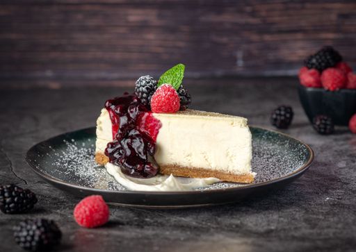 A close-up shot of a cheesecake served with berries and jam on a plate