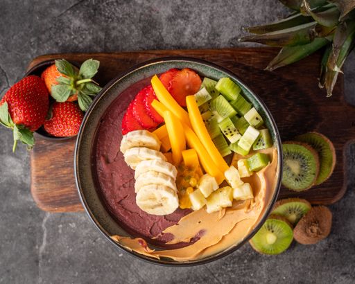 A top view of an acai bowl with tropical fruits and nuts on a wooden board