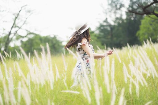 A female wearing a white floral dress in the middle of a grass covered field