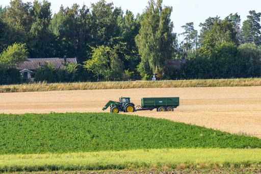 A Tractor out in the fields farming in the Swedish countryside. Agriculture with trees