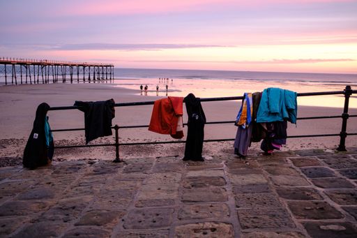 A sunset with clothing hung up on a metal fence with a scenic beach landscape in the background