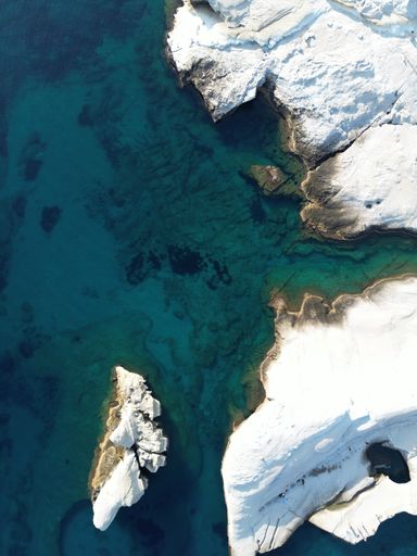 An aerial view of a white rocky coast on an island meeting a crystal-clear ocean on a sunny summer day