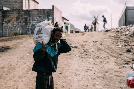 A South African male worker carrying a heavy load on his shoulder while standing in front of a dirt-filled area